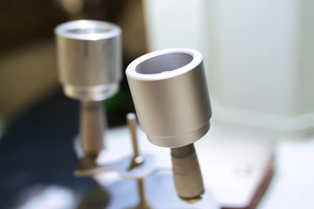 Bauteil während des Kugelstrahlens in Detailansicht Detailaufnahme eines einzelnen Aluminium-Bauteils mit runder Abdeckung im Kugelstrahlprozess.
